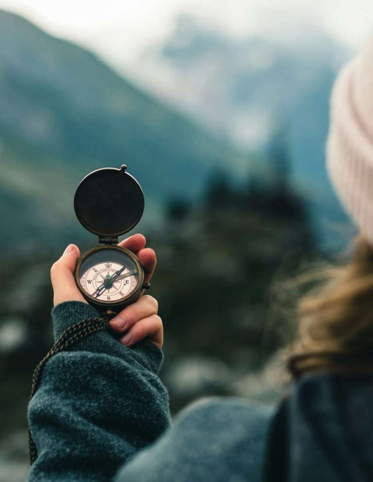 Eine Person hält einen Kompass vor einer nebligen Berglandschaft.